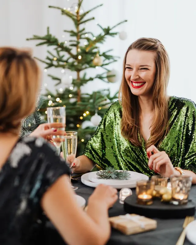 Lachende Frau im festlichen Kleid mit Sektglas vor dem Christbaum