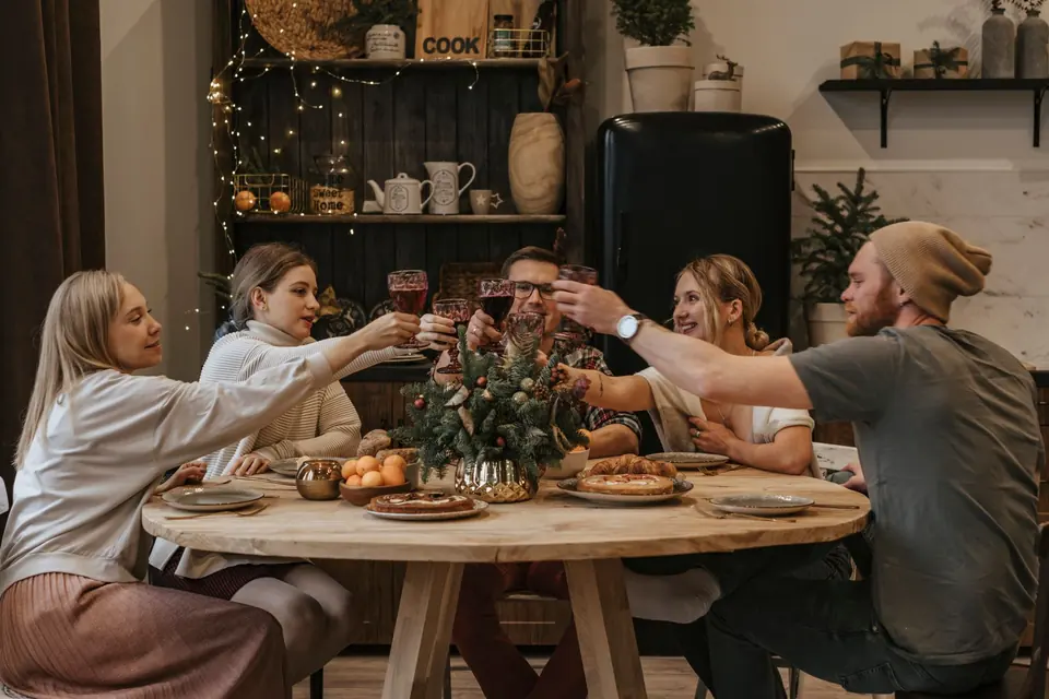 Gruppe stößt an einer weihnachtlich gedeckten Tafel lachend an
